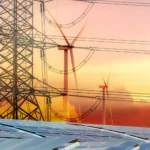 Imagen que muestra una torre de alta tensión junto a aerogeneradores y paneles solares, simbolizando la energía renovable y la sostenibilidad en un atardecer colorido.