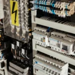 Panel eléctrico con componentes de control y protección, incluyendo interruptores automáticos y conexiones eléctricas, mostrando una señal de advertencia de alto voltaje.