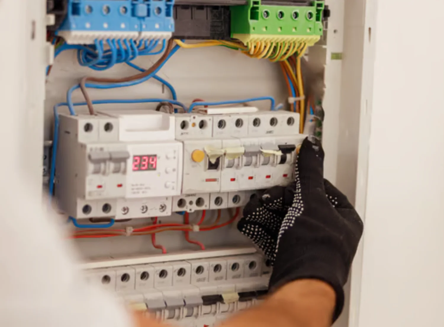 Técnico revisando un panel eléctrico, ajustando interruptores y medidores de voltaje en un entorno residencial.