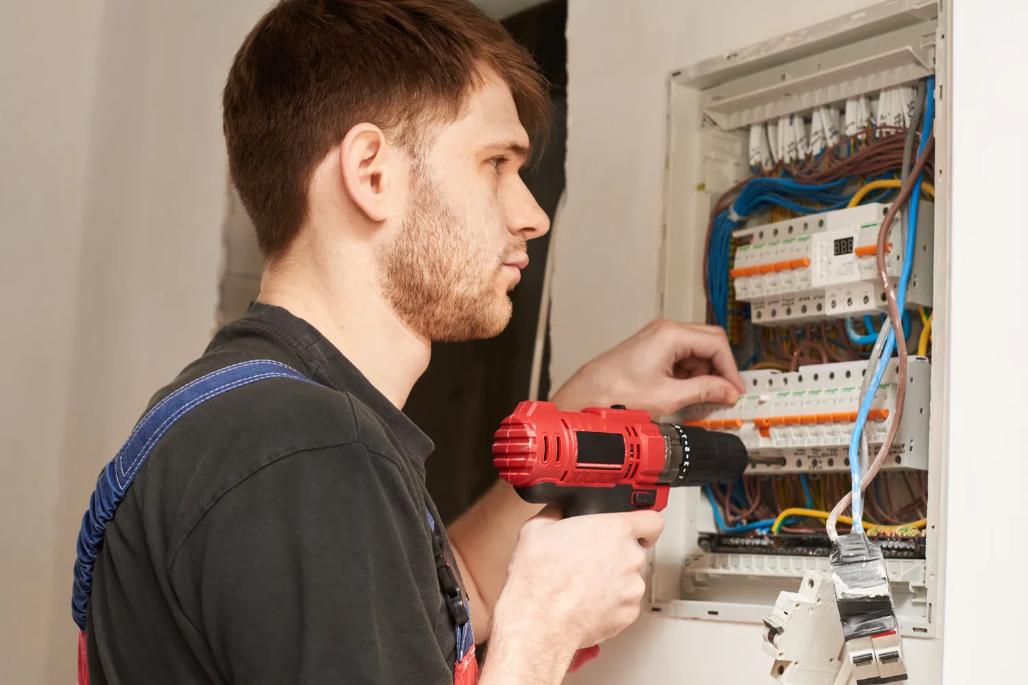 Técnico electricista trabajando en un panel eléctrico, usando un taladro rojo para realizar conexiones y ajustes en el cableado.
