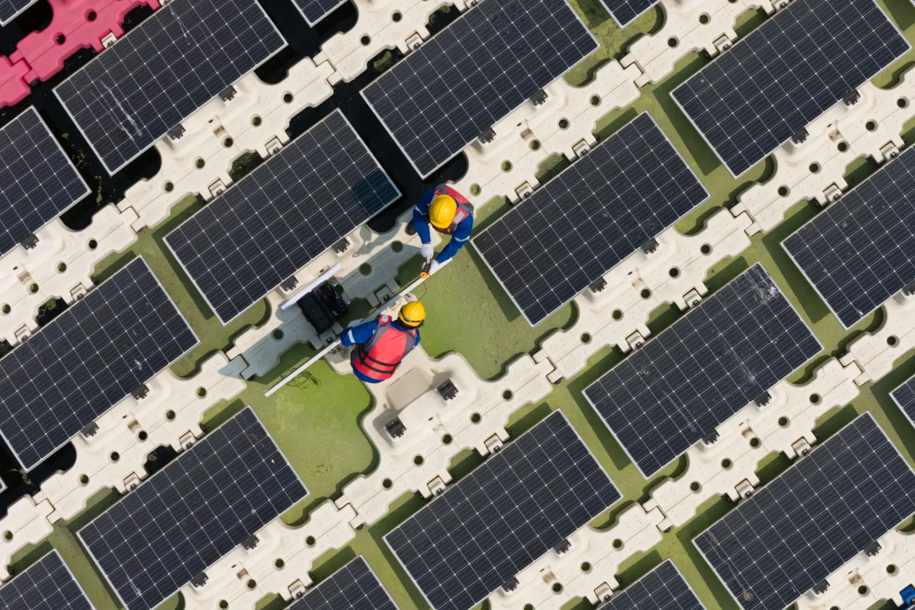 Trabajadores en una instalación solar, realizando mantenimiento en paneles fotovoltaicos desde una perspectiva aérea.