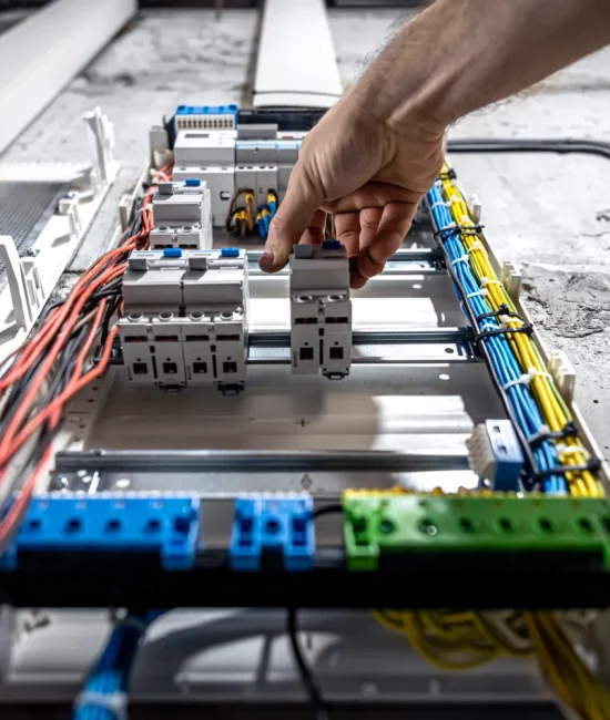 Técnico eléctrico instalando un disyuntor en un panel de distribución con cables organizados en colores.