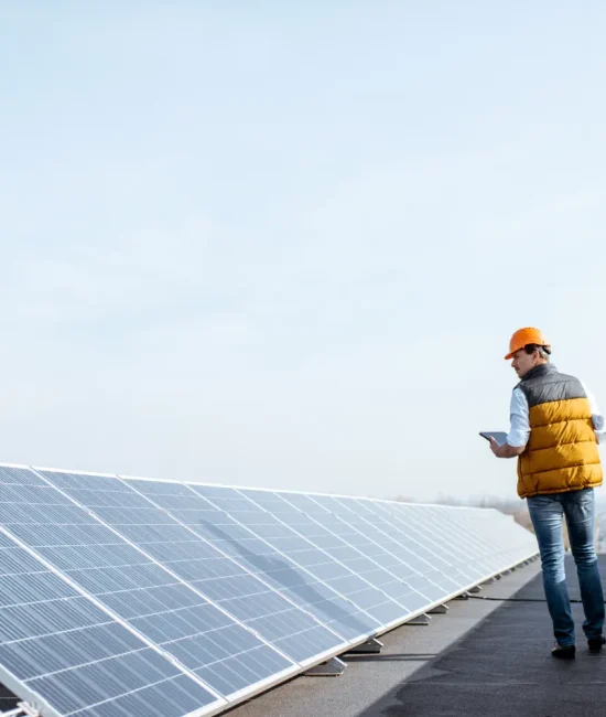 Técnico revisando paneles solares en un techo, usando una tablet, con un cielo despejado al fondo.